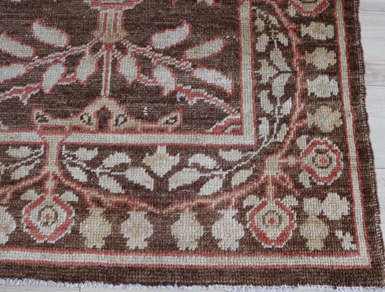 May include: A rectangular area rug featuring a deep brown background with a repeating floral and leaf pattern in shades of cream and muted coral. The design includes a wide border with stylized blossoms and foliage, finished with a short fringe.