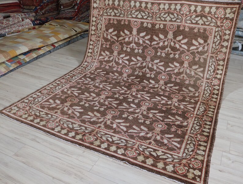 May include: A large rectangular area rug featuring a deep brown background with a repeating floral and vine pattern in cream and muted red. The rug has a wide decorative border with a similar botanical motif and a fringe along the edges.