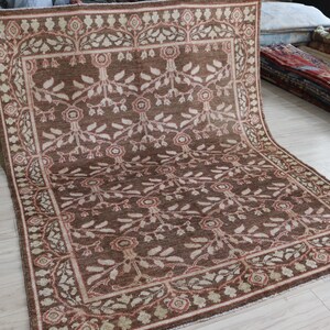 May include: A large rectangular area rug featuring a deep brown field with a repeating floral and vine pattern in cream and muted red. The rug is framed by a wide decorative border containing a continuous scrolling vine motif in matching colors.