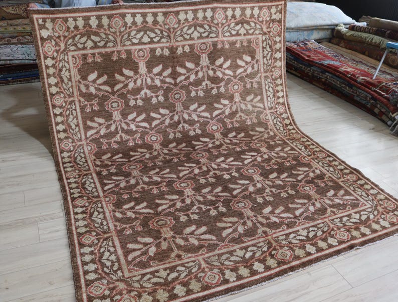 May include: A large rectangular area rug featuring a deep brown field with a repeating floral and vine pattern in cream and muted red. The rug is framed by a wide decorative border containing a continuous scrolling vine motif in matching colors.