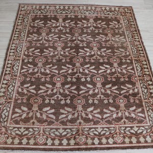 May include: A rectangular area rug featuring a dark brown background with a repeating floral and vine pattern in shades of cream, light pink, and muted red. The rug has a wide decorative border with a continuous leaf and flower motif.