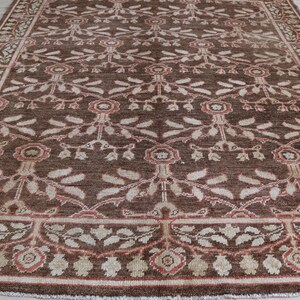 May include: A rectangular area rug featuring a deep brown background with a repeating floral and vine pattern in shades of cream, beige, and muted red. The design includes a central field of stylized blossoms and a decorative border frame.