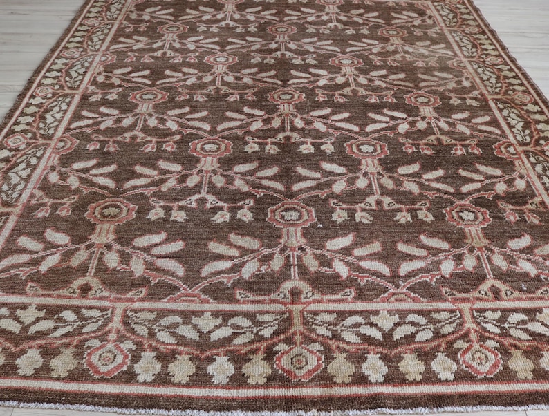 May include: A rectangular area rug featuring a deep brown background with a repeating floral and vine pattern in shades of cream, beige, and muted red. The design includes a central field of stylized blossoms and a decorative border frame.