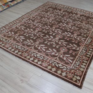 May include: A rectangular area rug featuring a dark brown background with a repeating pattern of light-colored floral motifs and leafy vines. The rug is framed by a decorative border containing smaller floral elements in shades of tan and red.