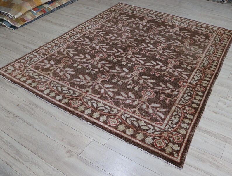 May include: A rectangular area rug featuring a dark brown background with a repeating pattern of light-colored floral motifs and leafy vines. The rug is framed by a decorative border containing smaller floral elements in shades of tan and red.