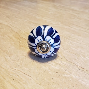 May include: A round cabinet knob with a white base and a blue floral design. The knob has a silver-colored metal base and screw. This decorative hardware is suitable for drawers and cabinets.