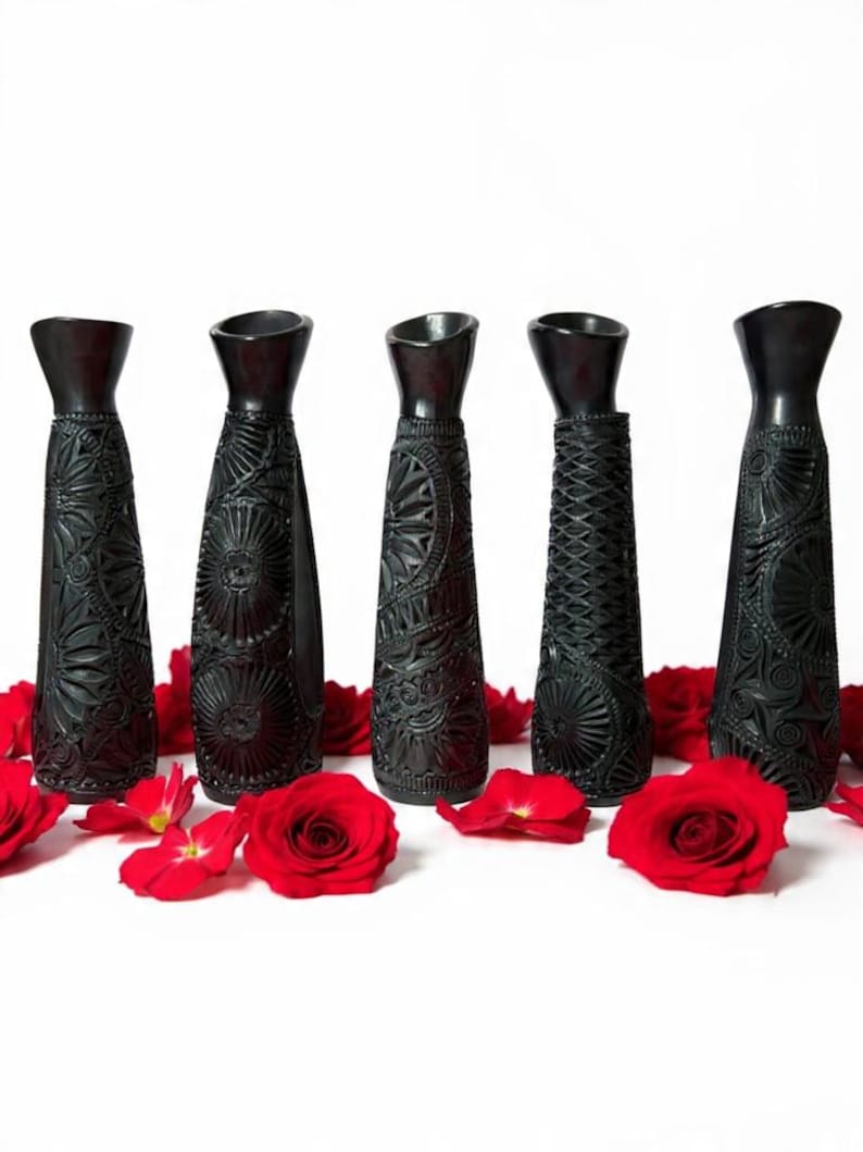 K&ouml;nnte beinhalten: F&uuml;nf schwarze dekorative Vasen mit aufwendigen Schnitzmustern, jede mit einem einzigartigen Muster. Rote Rosenbl&auml;tter und ganze Rosen sind um die Vasen auf wei&szlig;em Hintergrund verstreut. Die Vasen haben eine konische Form.