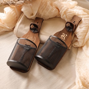 May include: Two wooden bottle-shaped wall-mounted bottle openers with black metal mesh storage. The wood has a natural finish, and the openers are made of dark metal. The design includes a bottle opener and a small storage basket.