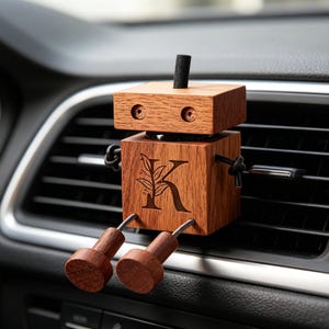 May include: A wooden robot-shaped car air freshener. The robot is made of light brown wood with a dark brown accent on top. The robot has a black string for arms and legs. The letter "K" and a leaf design are engraved on the front.