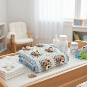 Puede incluir: Una manta de beb&eacute; hecha a mano, doblada, con un dise&ntilde;o azul y crema. La manta presenta cuadrados de ganchillo con aplicaciones de ositos de peluche marrones. Sobre una mesa para cambiar pa&ntilde;ales con art&iacute;culos para beb&eacute;s.