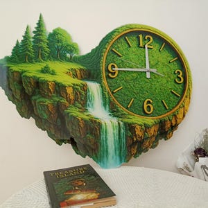 May include: A unique wall clock featuring a landscape design with a waterfall and trees. The clock face is green with gold numerals and hands. The clock is mounted on a white wall. The clock measures approximately 18 inches in diameter.