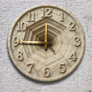 May include: A round wall clock with a unique design. The clock face is beige with a marble-like texture and features gold-colored hands. The numbers are raised and in a serif font. The clock has a tunnel-like design in the center.