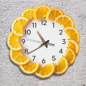 May include: A white wall clock with black numerals and gold hands. The clock face is surrounded by a decorative border of orange citrus slices, creating a unique and vibrant design. The clock is mounted on a textured, light gray wall.