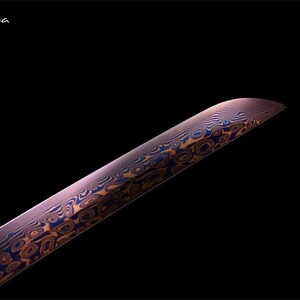 May include: Close-up of a blade with a unique pattern of swirling blue and gold designs on a purple background. The blade has a curved edge and is set against a black backdrop. The text "Flexi-casa" is in the upper left corner.