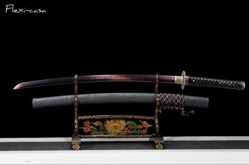 May include: A Japanese katana sword with a purple blade and black handle rests on a decorative stand. The scabbard is black with a textured pattern. The stand is black with gold accents and a floral design. The text "Flexi-casa" is in the upper left corner.