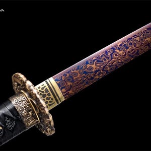 May include: Close-up of a Japanese katana sword with a patterned blade in shades of blue and gold. The hilt is wrapped in black material with ornate gold-colored metal fittings. The text "Flexi-casa" is in the upper left corner.