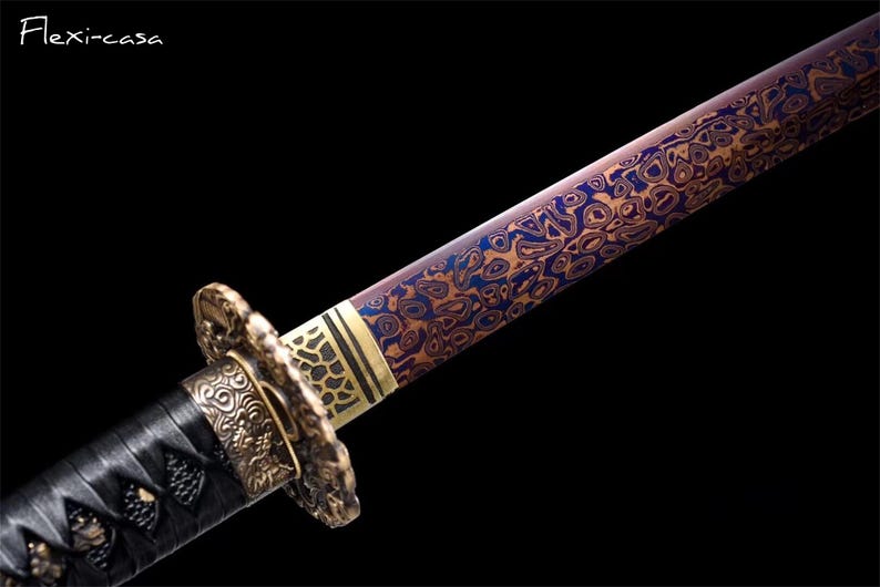 May include: Close-up of a Japanese katana sword with a patterned blade in shades of blue and gold. The hilt is wrapped in black material with ornate gold-colored metal fittings. The text "Flexi-casa" is in the upper left corner.