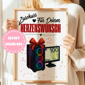 Puede incluir: Impresión digital enmarcada con una torre de ordenador negra con un lazo rojo, un monitor de ordenador que muestra un billete de 100 euros y el texto alemán "Zuschuss Für Deinen Herzenswunsch". Un círculo rosa con "SOFORT DOWNLOAD" está en la esquina inferior izquierda.