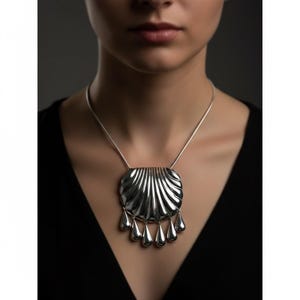 May include: A silver-toned pendant necklace featuring a large, textured, shell-shaped pendant with vertical lines and six teardrop dangles. The necklace is worn on a silver chain against a dark background.