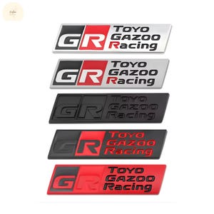 May include: A collection of five rectangular GR TOYO GAZOO Racing emblems in various color schemes. The emblems feature the letters "GR" in white or red, and the words "TOYO GAZOO Racing" in black or red.