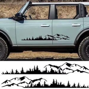 Puede incluir: Un adhesivo de vinilo negro que presenta la silueta de una cordillera y un denso bosque de pinos. El diseño se muestra aplicado en el lateral de un SUV azul claro y también como dos tiras horizontales separadas sobre un fondo blanco.