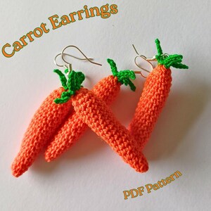 Op de afbeelding: Handgemaakte oranje gehaakte wortel oorbellen met groene toppen. De oorbellen worden gepresenteerd op een wit oppervlak. De tekst "Carrot Earrings" en "PDF Pattern" zijn zichtbaar in de afbeelding.