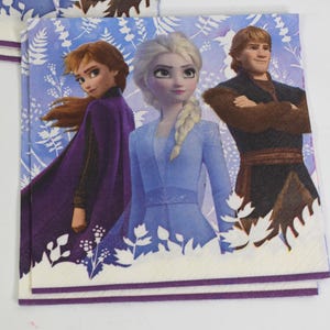 Pode incluir: Guardanapos de papel quadrados com personagens do filme de anima&ccedil;&atilde;o Frozen. Os guardanapos exibem Anna, Elsa e Kristoff contra um fundo floral azul e branco. Os guardanapos t&ecirc;m uma borda branca com uma faixa roxa.