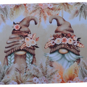 May include: Two brown gnomes with white beards wearing brown hats with floral accents. The gnomes are surrounded by beige and brown palm leaves and flowers.