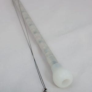May include: A white, translucent, cylindrical wand with a rounded tip and a black cord. The wand has a textured grip and appears to contain small, colored lights. The cord has a small, silver-colored charm at the end.