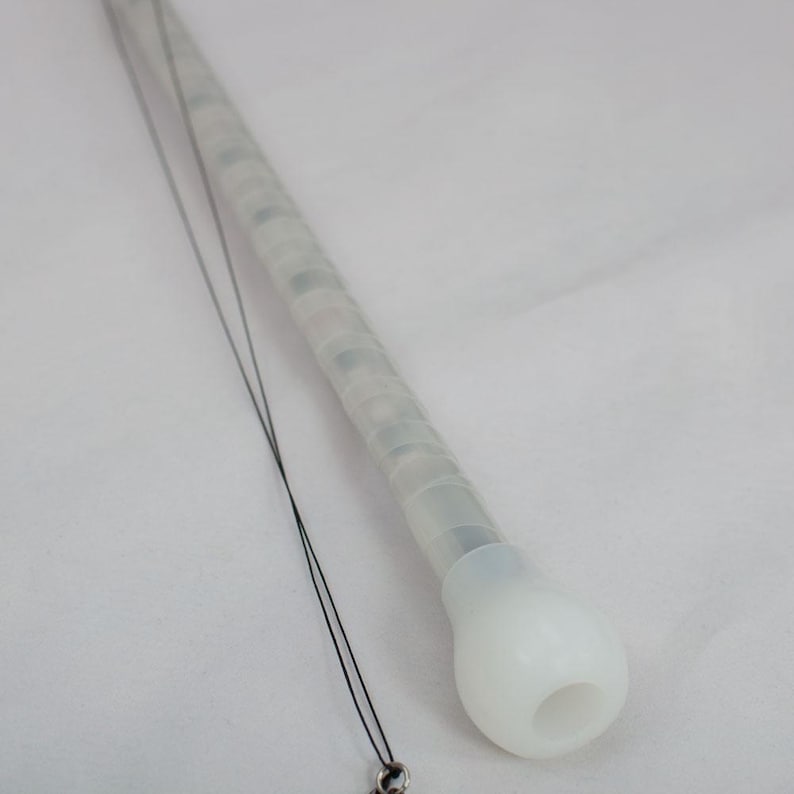 May include: A white, translucent, cylindrical wand with a rounded tip and a black cord. The wand has a textured grip and appears to contain small, colored lights. The cord has a small, silver-colored charm at the end.