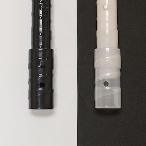 May include: Close-up of two shelf support poles. One is black, the other is clear. Both have a cylindrical design with a series of ridges and a circular hole. The black pole is on a white background, and the clear pole is on a black background.