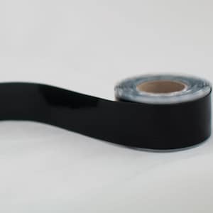 May include: A roll of black electrical tape with a glossy finish. The tape is partially unrolled, revealing the cardboard core. The background is plain white.