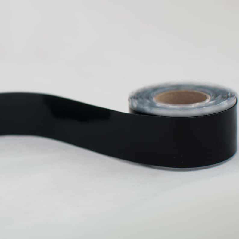 May include: A roll of black electrical tape with a glossy finish. The tape is partially unrolled, revealing the cardboard core. The background is plain white.