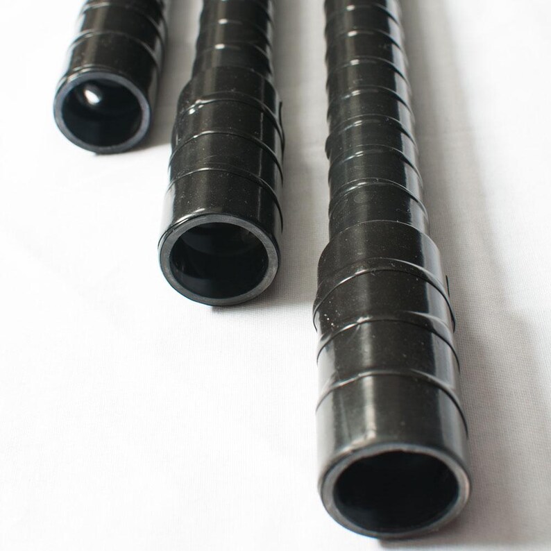 May include: Close-up of three black plastic tubes of varying lengths. The tubes have a ridged, spiral design and open ends, revealing a hollow interior. The tubes are set against a white background.