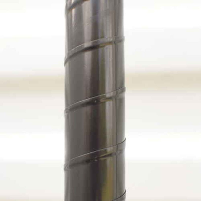 May include: A close-up of a dark gray metal pole with a spiral design. The pole has a glossy finish and is set against a blurred white background. The spiral detail adds a decorative element to the pole.