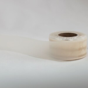 May include: A roll of clear, semi-transparent tape with a brown cardboard core. The tape is partially unrolled, showing a length of the adhesive material. The background is plain white.
