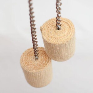May include: Two beige fire poi heads, each rolled and attached to a silver chain. The cylindrical heads are made of a woven material. The background is a soft, neutral color.