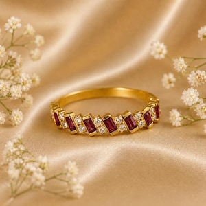 May include: A gold band ring featuring an alternating pattern of rectangular baguette-cut red rubies and small round brilliant-cut white diamonds set in a continuous row around the circumference of the metal band.