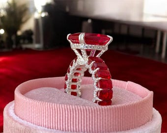 Peut inclure: Gros plan d'une bague en rubis posée dans un écrin en velours rose. La bague présente une grosse pierre centrale en rubis rectangulaire et de plus petits rubis sertis le long de l'anneau. La bague est entourée de petites pierres d'accent claires.