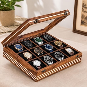 May include: A rectangular wooden watch display case with a hinged glass lid and metal latches. The interior features twelve individual compartments lined with black fabric, each containing a different analog wristwatch with various dial colors.