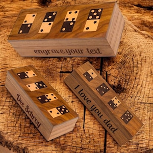 May include: Wooden domino sets with engraved text. The sets feature black and white domino tiles inlaid into the wooden boxes. One box reads "engrave your text", another reads "Dee Schroy", and the third reads "I love you dad".