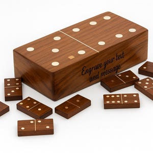 May include: A wooden domino set with a matching box. The dominoes and box are a dark brown color with white dots. The box has the text "Engrave your text and message".