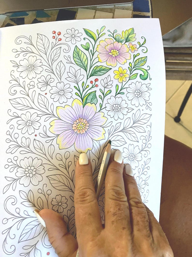 May include: A partially colored floral coloring book page with a hand holding a colored pencil. The flowers are colored in shades of pink, yellow, and purple, with green leaves and red berries. The rest of the flowers are uncolored.