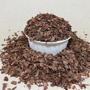 Peut inclure: Un bol en céramique blanc rempli d'écorce de bois brune, entouré d'une pile du même matériau. Les morceaux de paillis varient en taille et en forme, créant un aspect texturé. Idéal pour le jardinage et l'aménagement paysager.