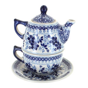 May include: A blue and white ceramic tea set featuring a teapot, teacup, and saucer. The set is decorated with a floral pattern in shades of blue. The teapot sits atop the teacup, which rests on the saucer. The set is designed for one person.