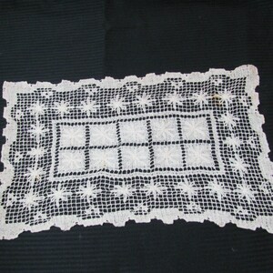 May include: White crocheted doily with a square pattern in the center and a floral design around the border.