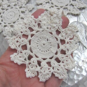 May include: Off-white, handmade crochet doilies. The doilies feature a central circular design with an open, lacy pattern radiating outwards. The crochet work is detailed and intricate, showcasing the texture of the yarn.