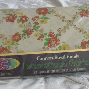 May include: A white twin fitted bottom sheet with a floral print in shades of red, yellow, and green. The sheet is packaged in plastic and has a label that reads "Cannon Royal Family International Fashions. Twin fitted bottom sheet for 39 x 76 in mattress. No-iron percale."