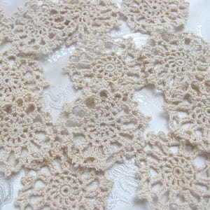 Peut inclure: Gros plan de plusieurs napperons au crochet beiges avec un motif floral. Les napperons sont disposés sur une surface blanche et texturée. Les pièces crochetées présentent un motif ajouré délicat.