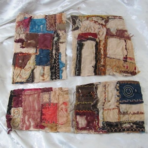 May include: Four handmade fabric pieces with a patchwork design. Each piece features a variety of colors including red, blue, brown, and beige. The fabrics are stitched together with visible thread, creating a textured, artistic appearance.